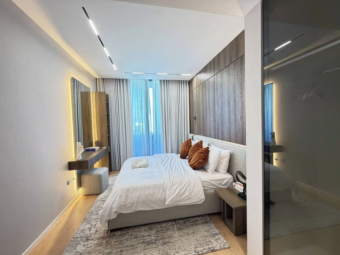 A modern bedroom with a large bed, a bedside table, a mirror, and a wardrobe.