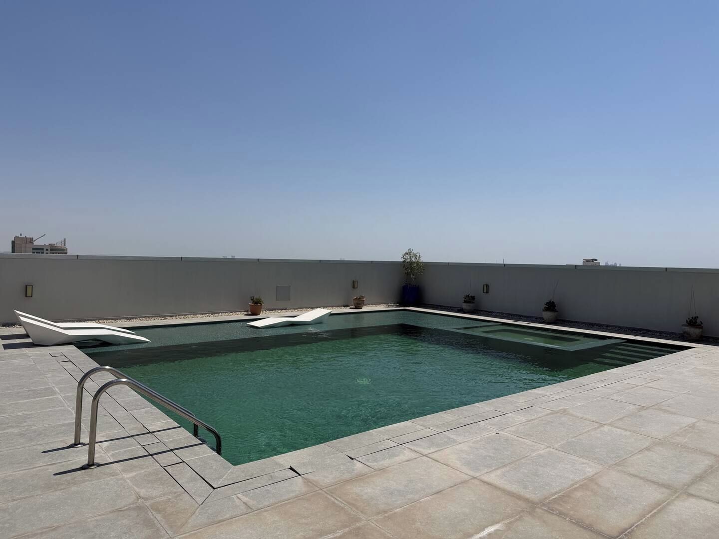A rooftop swimming pool with clear water, surrounded by a tiled deck and potted plants.