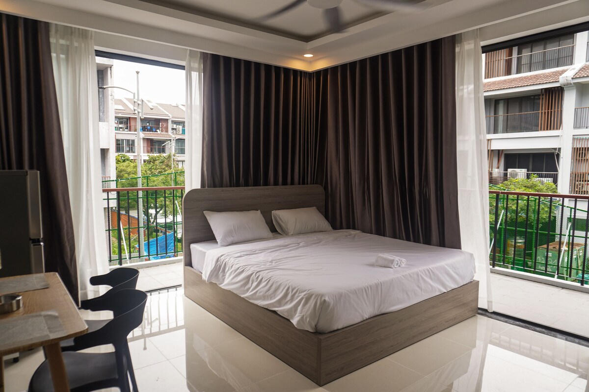 Ein Hotelzimmer mit Bett, Schreibtisch und Stuhl. Es gibt einen Balkon mit Blick auf Gebäude und Grünflächen.