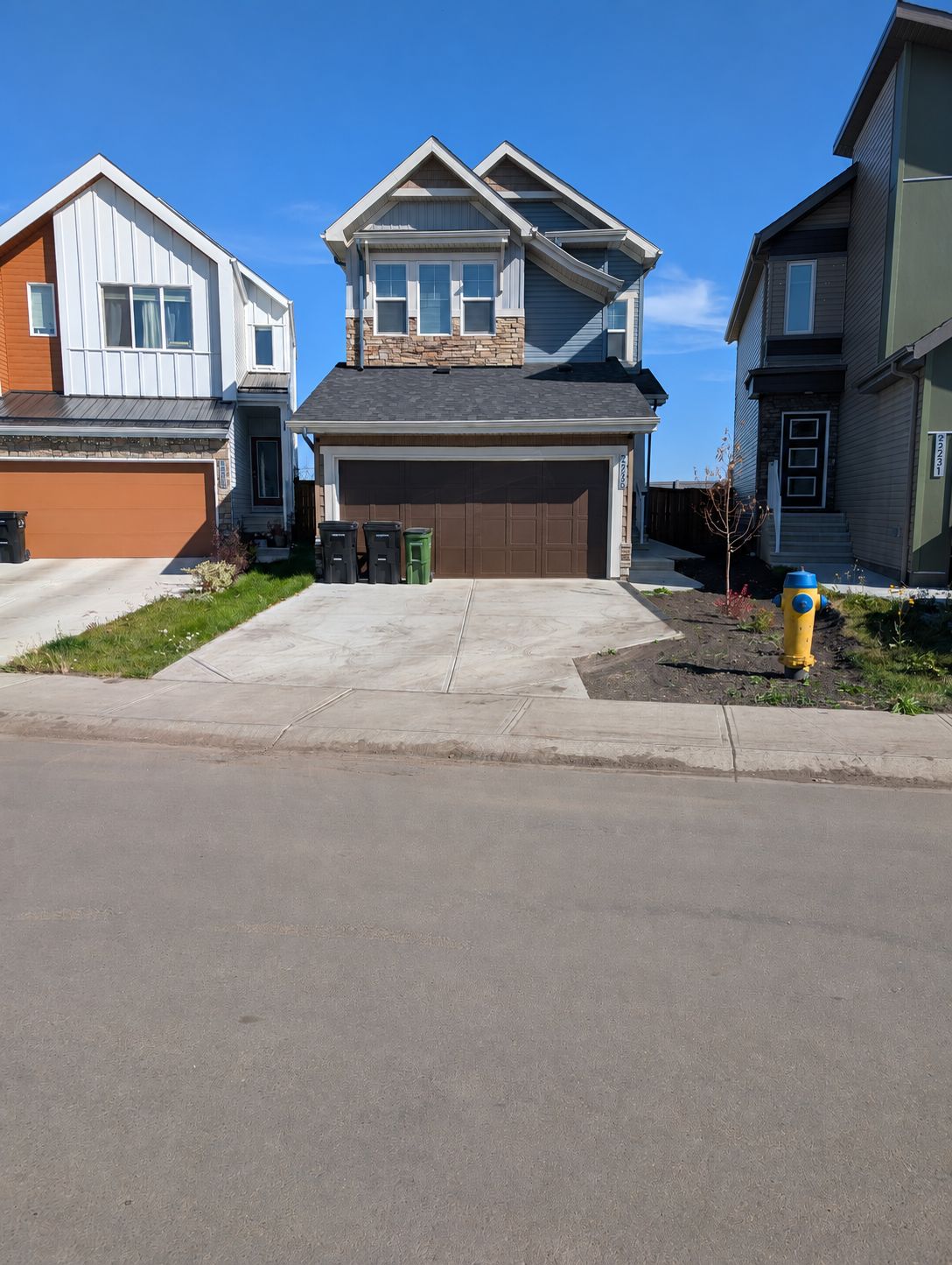 A residential street with houses featuring modern architecture, a garage, and a fire hydrant.