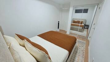 A bedroom with a bed, pillows, a bedside table, a mirror, and a sliding door leading to another room.