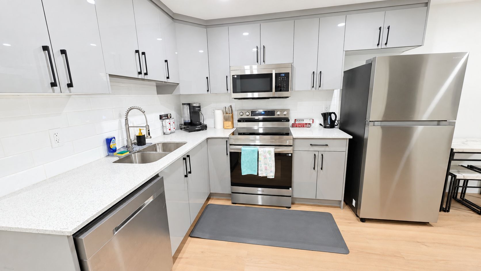 A modern kitchen with stainless steel appliances, white cabinetry, and a grey countertop.