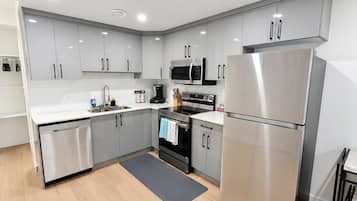 A modern kitchen with stainless steel appliances, white cabinetry, and a wooden floor.