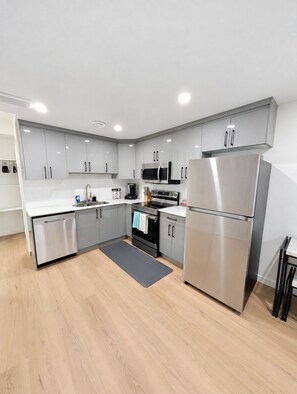 A modern kitchen with stainless steel appliances, white cabinetry, and a wooden floor. - Cozy Private Suite | Near WEM | No Cleaning Fee (Edmonton)