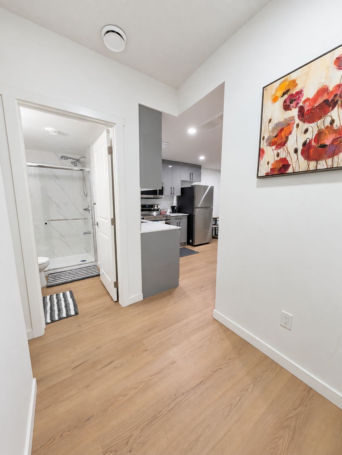A modern kitchen with grey cabinets, a stainless steel refrigerator, and a wooden floor.