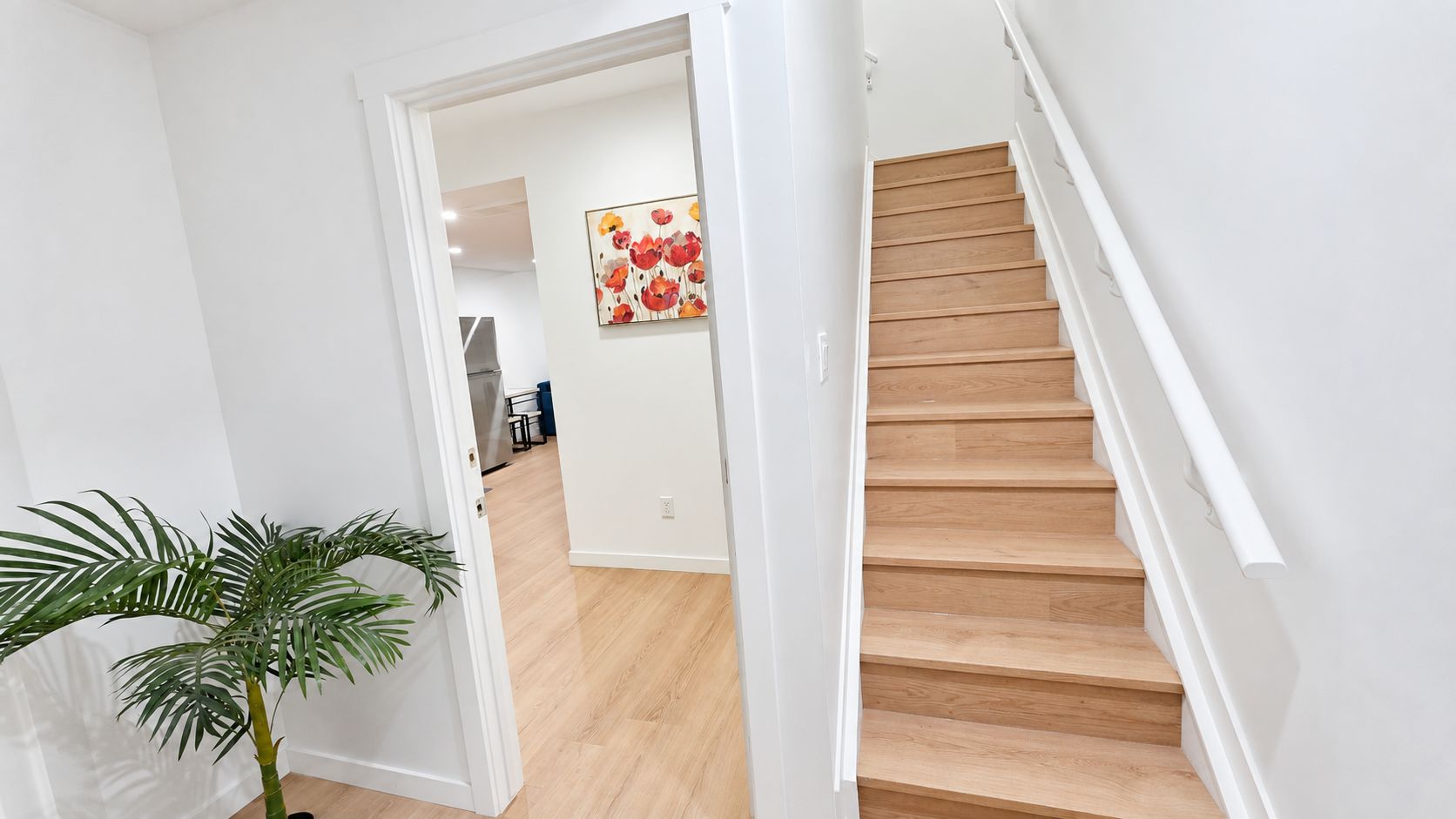 A staircase leading to a second floor with a wooden finish, a white wall, and a plant in the foreground.
