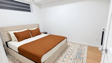 A bedroom with a bed, a nightstand, a patterned rug, and a window with blinds.