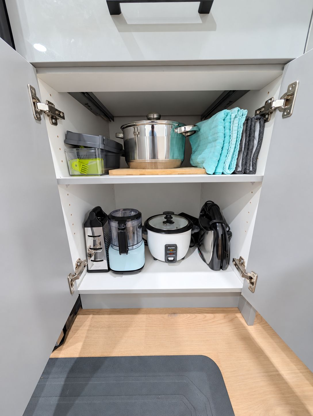 A kitchen with a built-in oven, a slow cooker, a rice cooker, and a pot on the countertop.