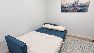 A bedroom with a bed, a bench, a patterned rug, and a wall with three paintings.