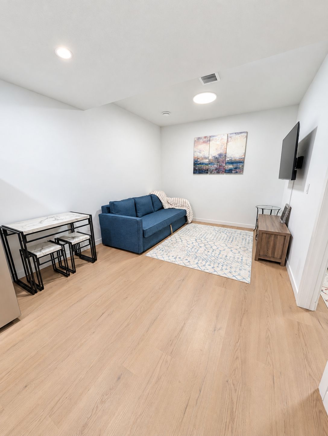 Un salon moderne comprenant un canapé, une table à manger avec des chaises, un téléviseur à écran plat fixé au mur et un tapis à motifs.