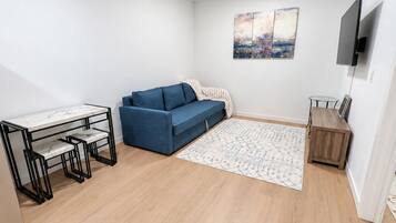 Un salon moderne comprenant un canapé, une table à manger avec des chaises, un téléviseur à écran plat fixé au mur et un tapis à motifs.