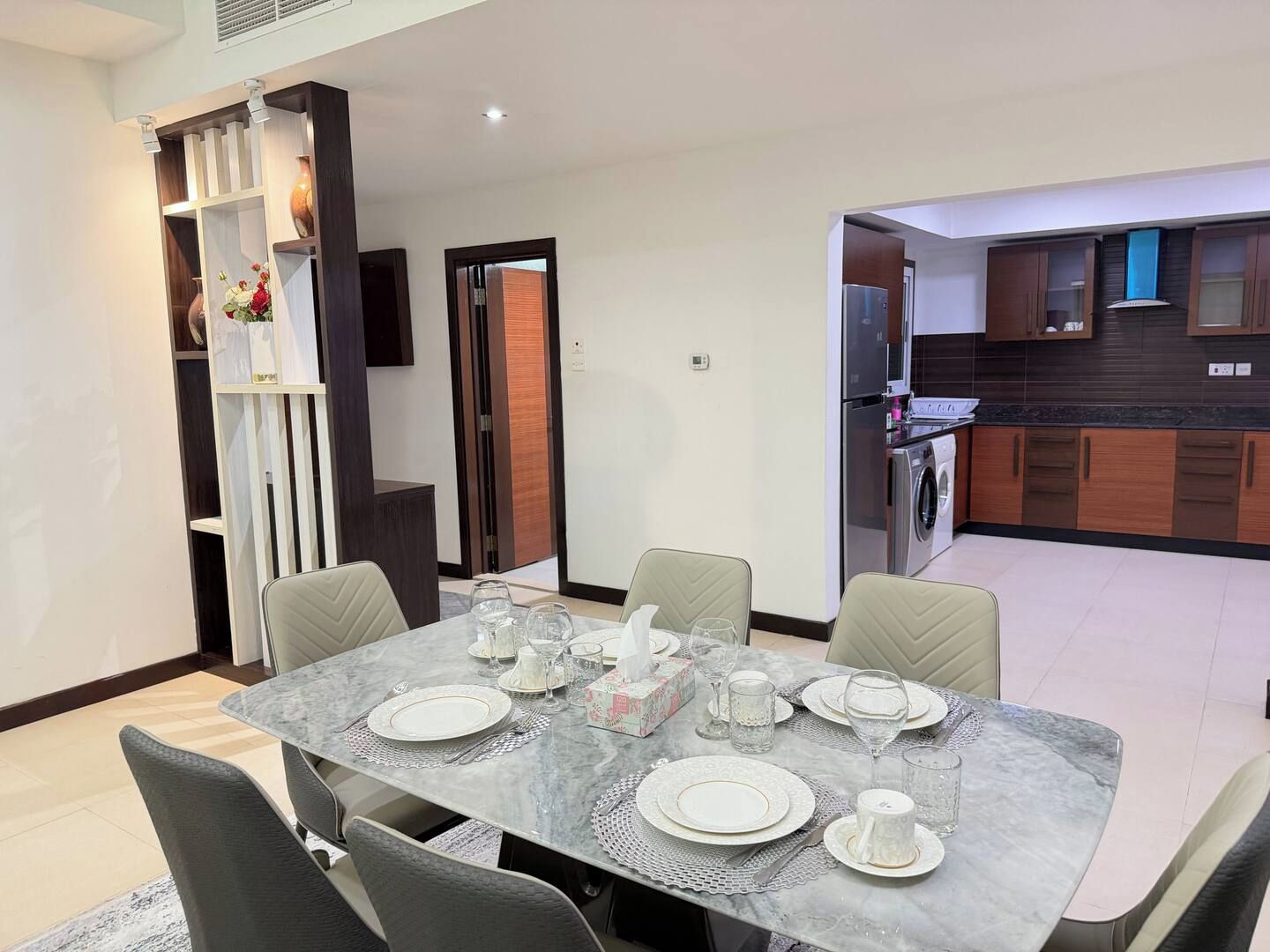 A dining area with a marble table set for four, a kitchen with modern appliances, and a separate dining room with a TV.