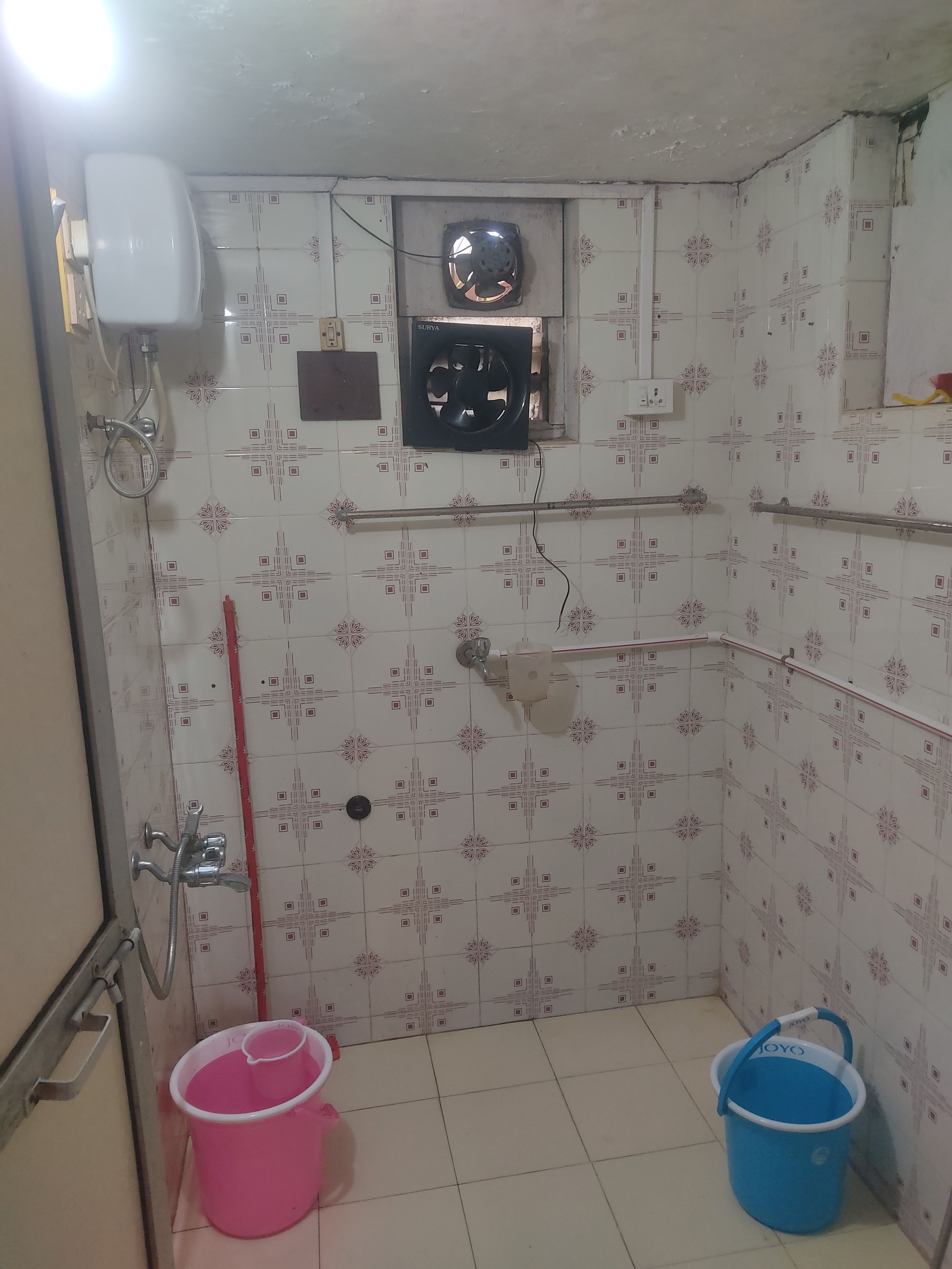 Une salle de bain avec des carreaux décorés, une douche, des toilettes, un ventilateur et un seau.