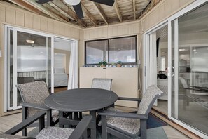 Een terras buiten met een ronde tafel en stoelen, een plafondventilator en schuiframen.