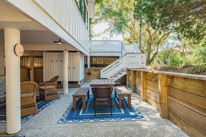 Eine überdachte Terrasse im Freien mit einem Holztisch und -stühlen, einem blauen Teppich mit Muster und einer Treppe, die zu einer oberen Ebene führt.