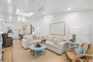 Un salon spacieux avec un canapé blanc, une table basse ronde et un fauteuil en osier.