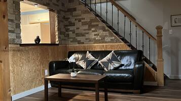 A living room with a wooden floor, a black leather sofa, a wooden coffee table, and a ceiling fan.