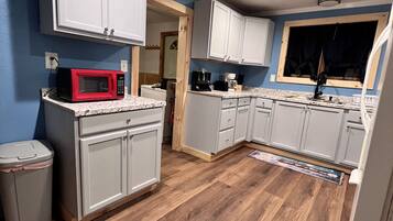 A kitchen with white cabinets, a red microwave, and a wooden floor.