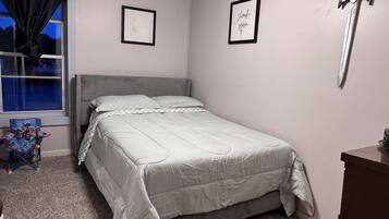 Un dormitorio con cama, ventilador de techo, ventana con cortinas, un cuadro enmarcado y una espada en la pared.
