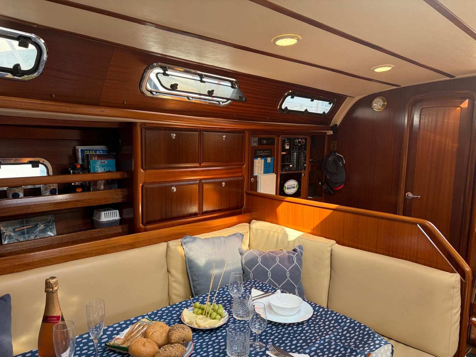 A boat cabin with a dining area featuring a table set for two, a cushioned bench, and a wooden cabinet with various items.
