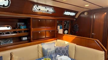 A boat cabin with a dining area featuring a table set for two, a cushioned bench, and a wooden cabinet with various items.