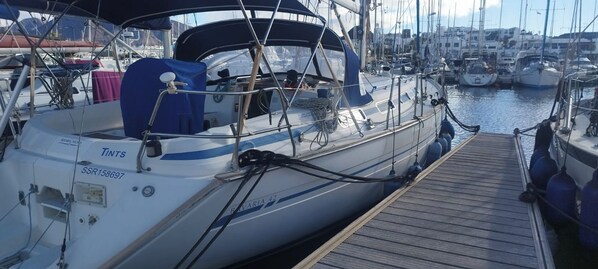 A sailboat docked at a marina with a wooden deck and other boats in the background.
