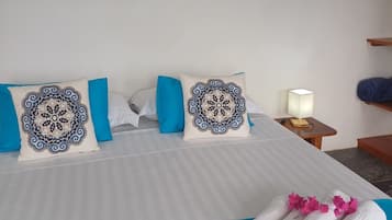 Habitación de hotel con cama, almohadillas decorativas, una obra de arte enmarco de una ballena, mesita de noche con lámpara y cama bien hecha con toallas.