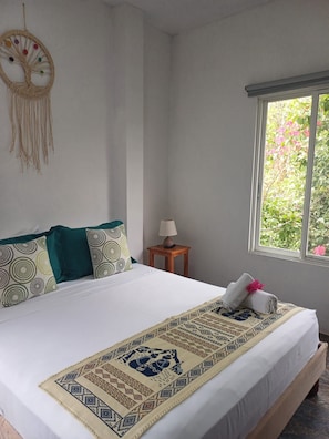 Un lit bien fait, recouvert d’une couvre-lit à motifs, avec deux oreillers ornés de motifs circulaires, une décoration murale et une fenêtre donnant sur un paysage verdoyant.