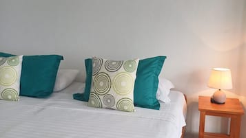 Una habitación de hotel con una cama, almohadas, una mesita de noche con una lámpara, un cuadro en la pared y una toalla con flores sobre la cama.