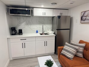 A compact kitchenette with a microwave, refrigerator, and white cabinets.