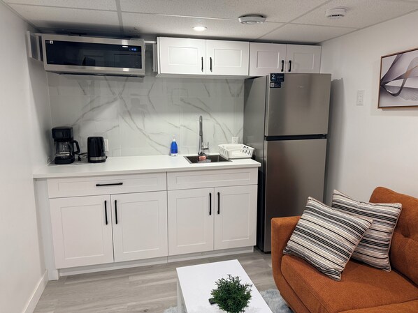 A compact kitchenette with a microwave, refrigerator, and white cabinets.