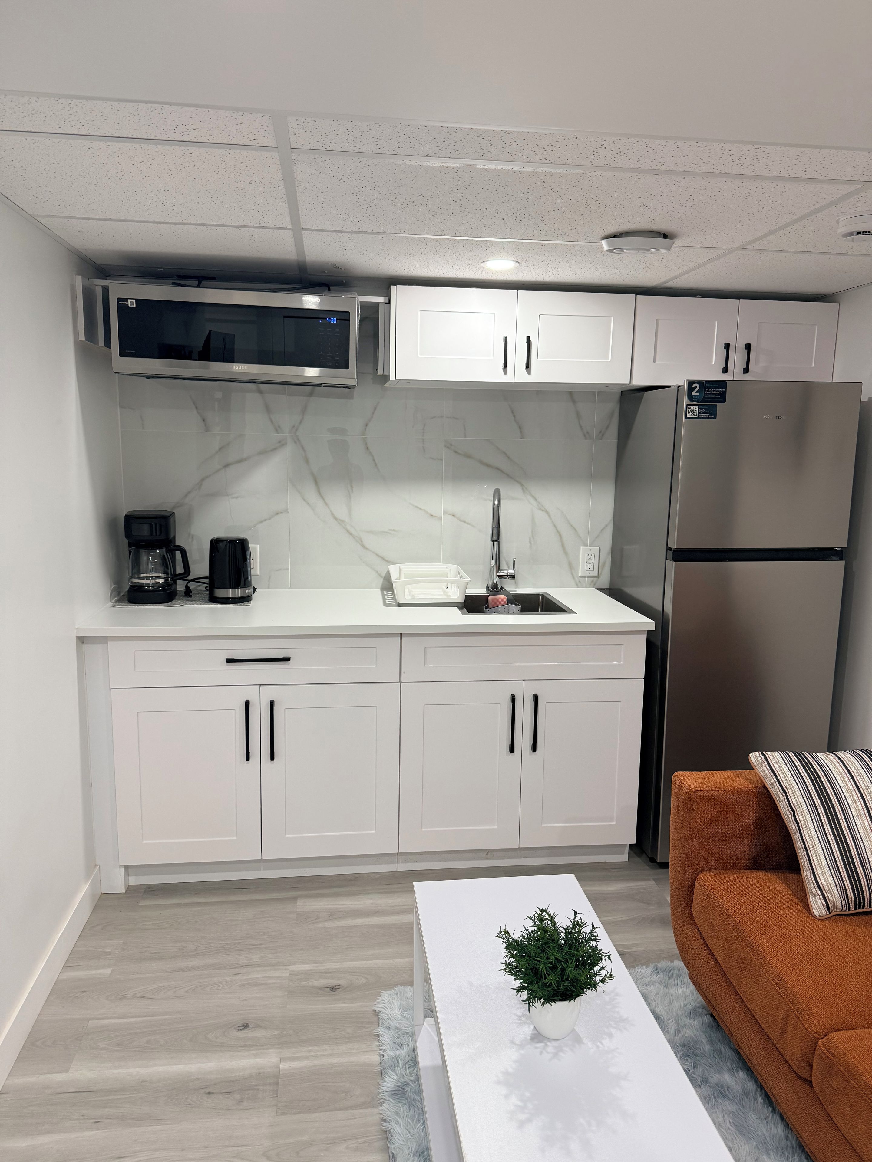 A modern kitchen with white cabinets, a stainless steel refrigerator, a microwave, and a coffee maker.