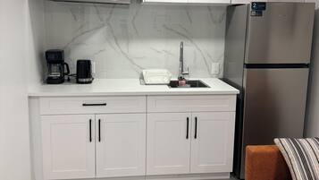 A modern kitchen with white cabinets, a stainless steel refrigerator, a microwave, and a coffee maker.