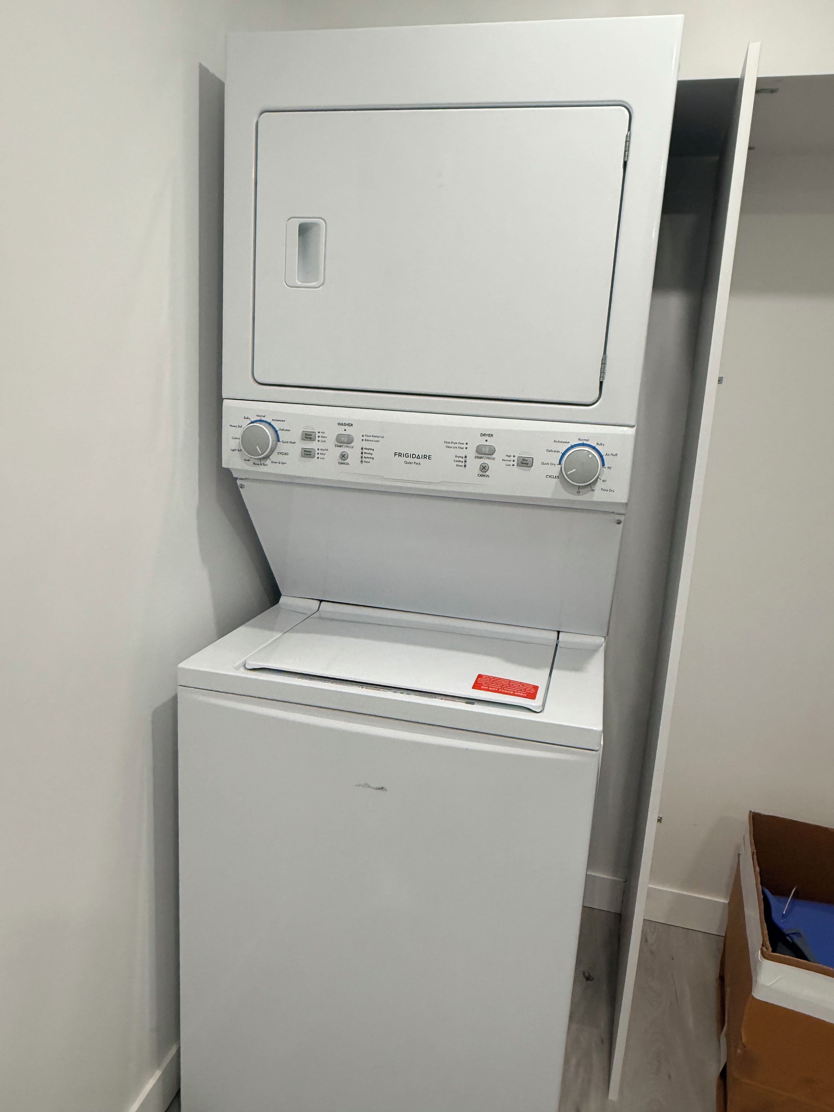 A compact, white, wall-mounted washer and dryer unit with control knobs and a red warning label.