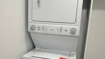 A compact, white, wall-mounted washer and dryer unit with control knobs and a red warning label.