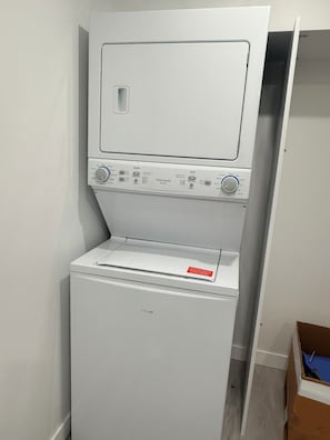 A compact, white, wall-mounted washer and dryer unit with control knobs and a red warning label.