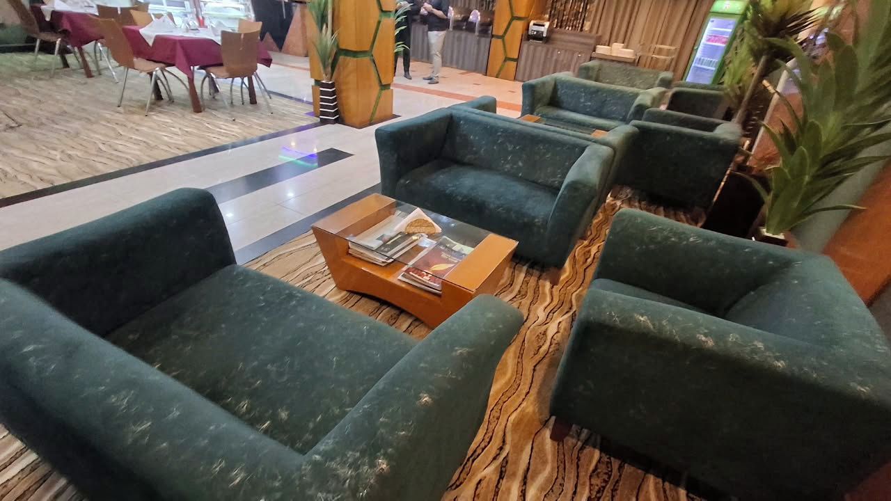 A lobby area with green upholstered sofas, a coffee table with magazines, and a patterned carpet.