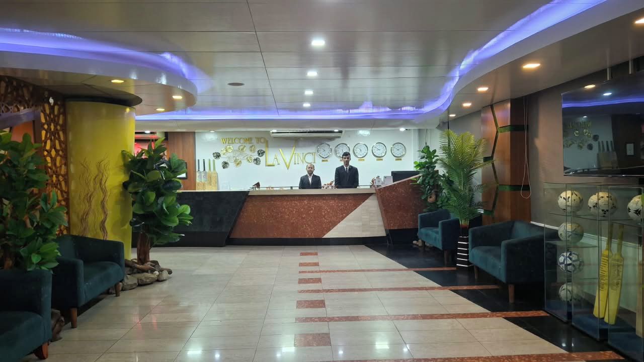 Een hotel receptie met een receptiebalie, twee baliemedewerkers en zithoekjes.