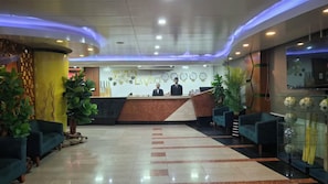 A hotel reception area with a reception desk, two receptionists, and seating arrangements.