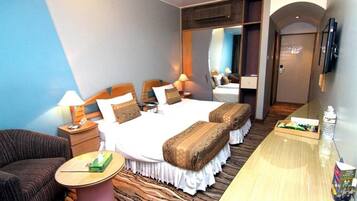 A hotel room with a bed, a sofa, a small table, a mirror, and a TV.