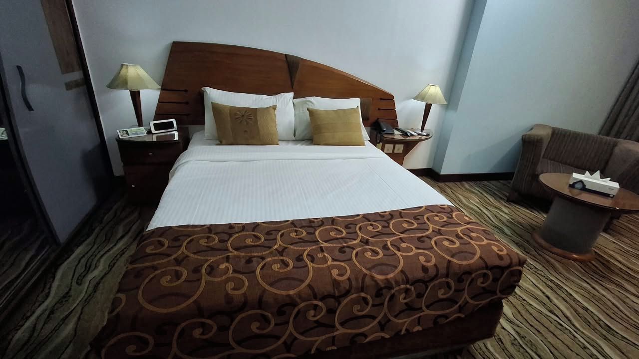 Een hotelkamer met een groot bed, twee nachtkastjes met lampen, een stoel en een kleine tafel met een afstandsbediening.