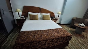 A hotel room with a large bed, two bedside tables with lamps, a chair, and a small table with a remote control.