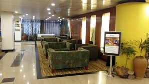 A hotel lobby with seating areas, a reception desk, and a signboard.