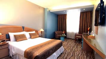 Une chambre d’hôtel équipée d’un lit, d’un bureau, d’une chaise, d’une télévision et d’une fenêtre avec des rideaux.