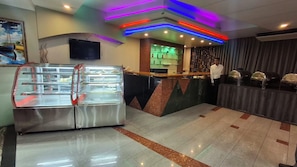 A hotel lobby with a reception desk, a food display case, and a bar area.