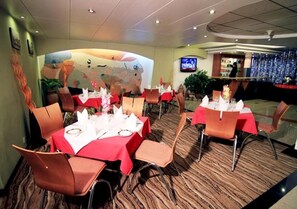 Un restaurante con mesas redondas, manteles rojos y sillas naranjas.