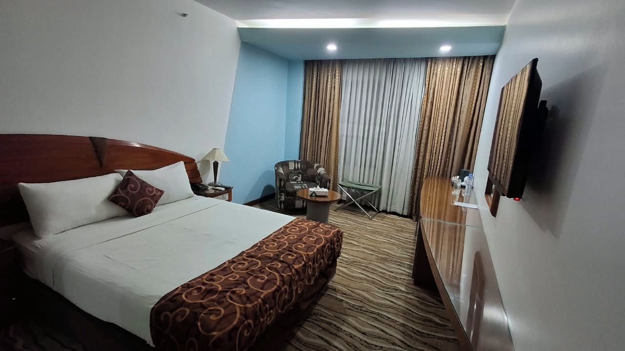 A hotel room with a bed, a desk, a chair, a TV, and a window with curtains.