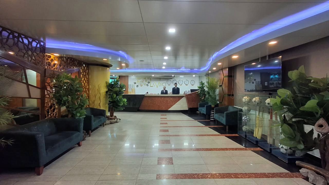Un vestíbulo de hotel con mostrador de recepción, sofás, plantas en macetas y un televisor.