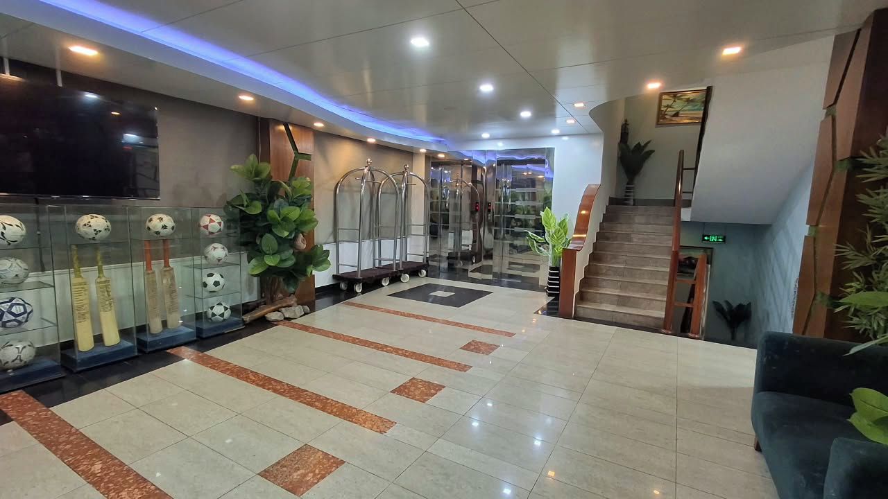 A hotel lobby with a tiled floor, a staircase, and a television mounted on the wall.