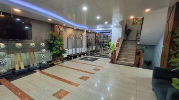 A hotel lobby with a tiled floor, a staircase, and a television mounted on the wall.